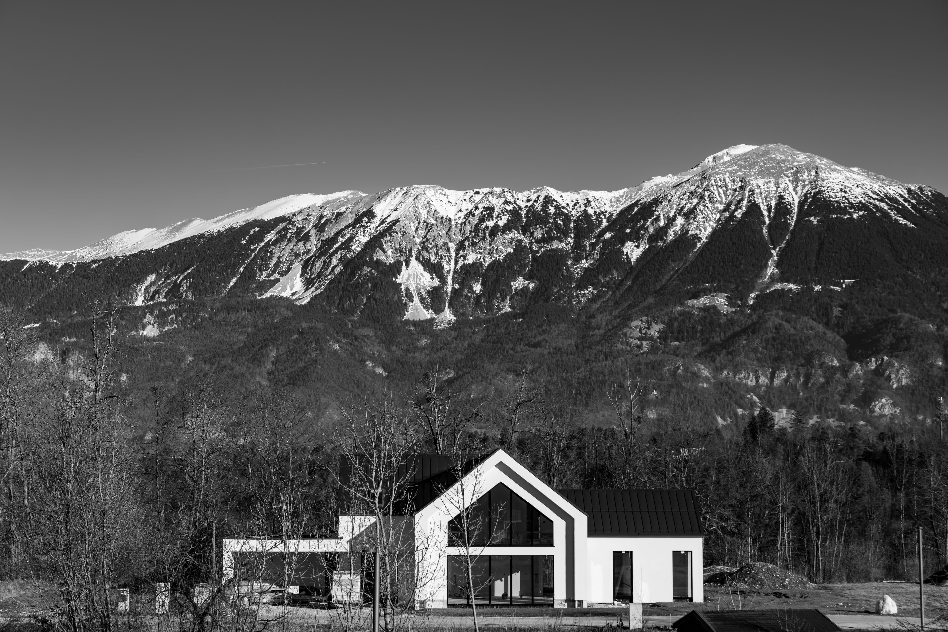 A gabled mountain-modern house below a snow-capped ridge