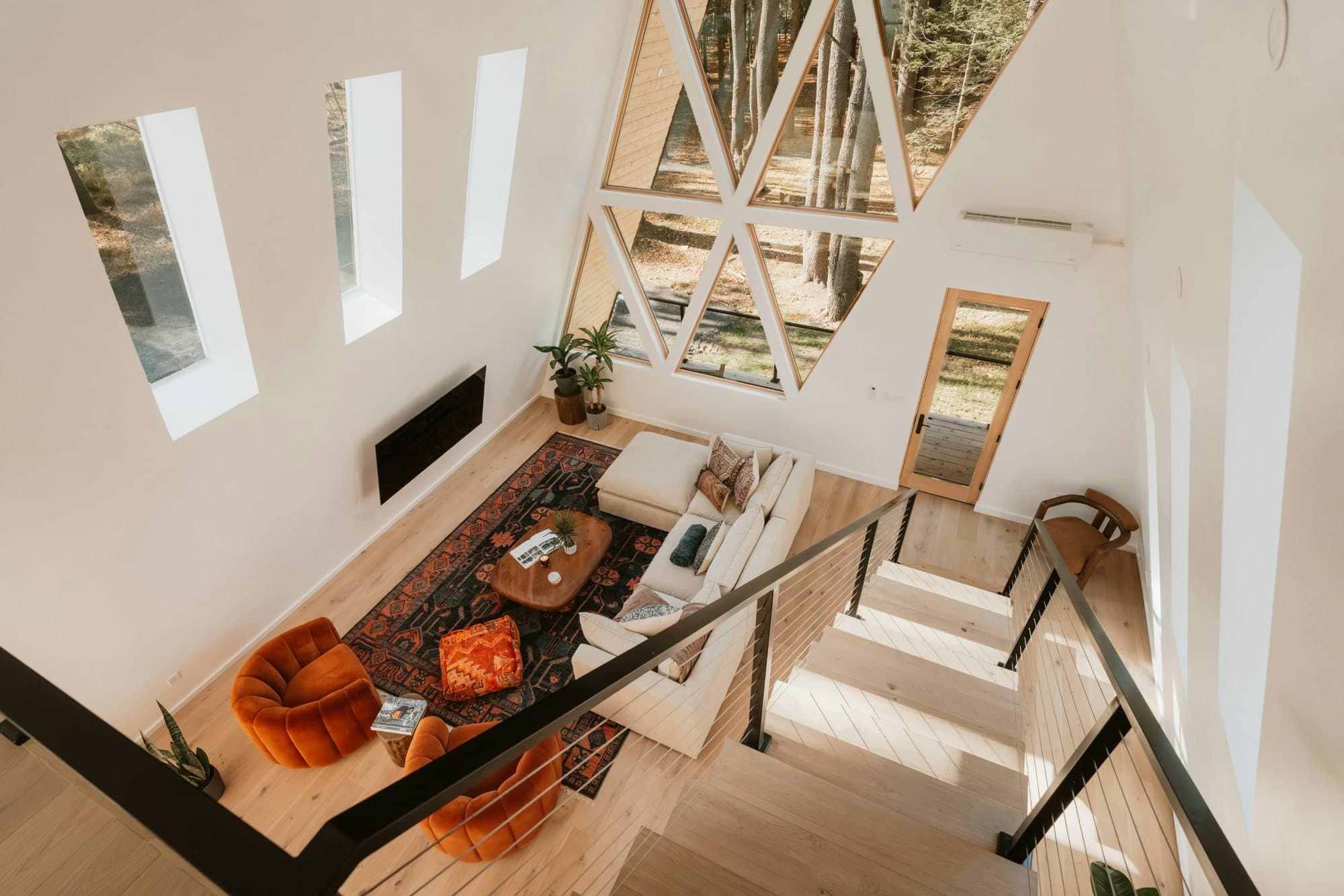 A double-height living room beneath an A-frame glazed gable, facing the trees