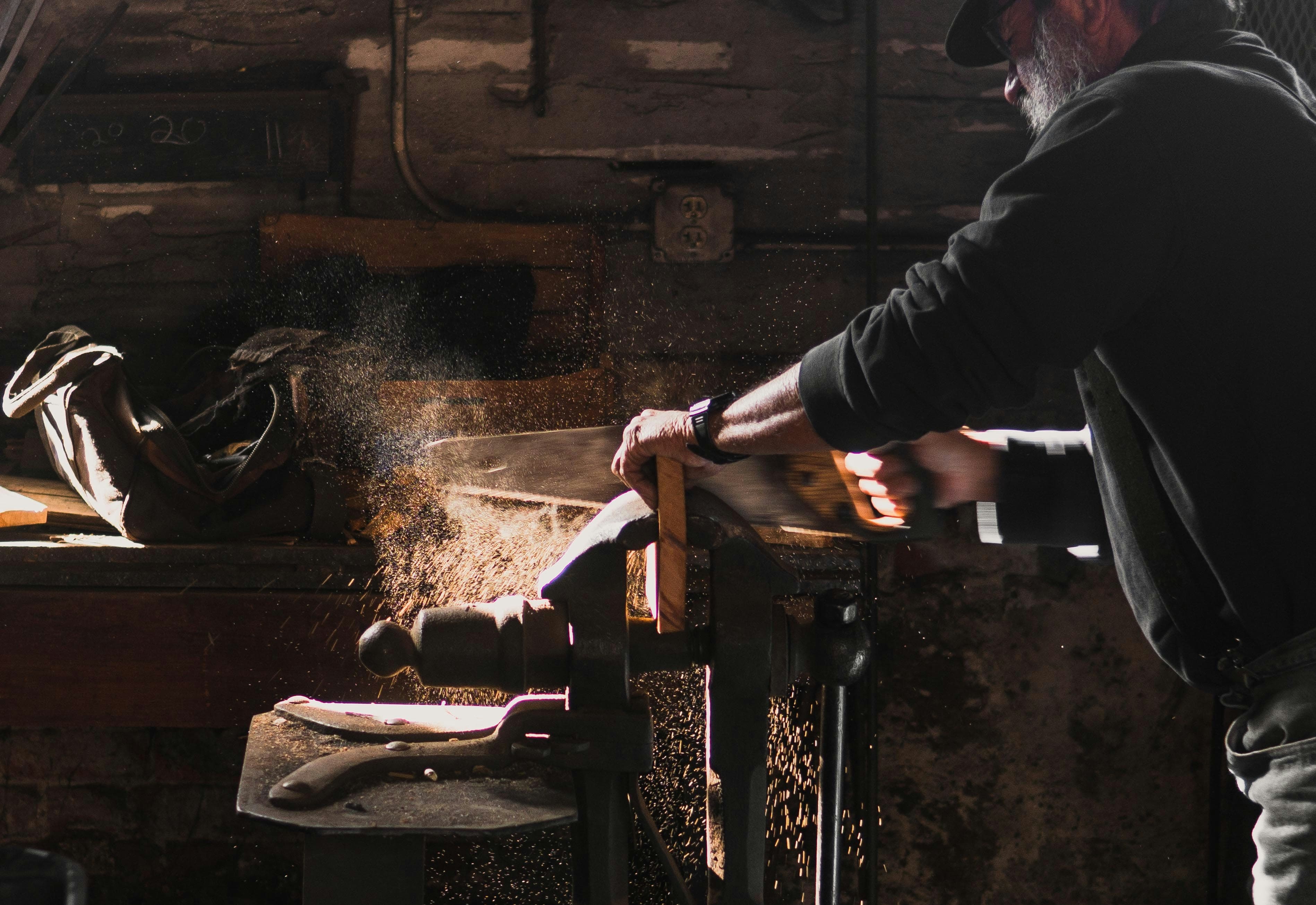 A craftsman sawing timber by hand in a workshop, sparks catching the light
