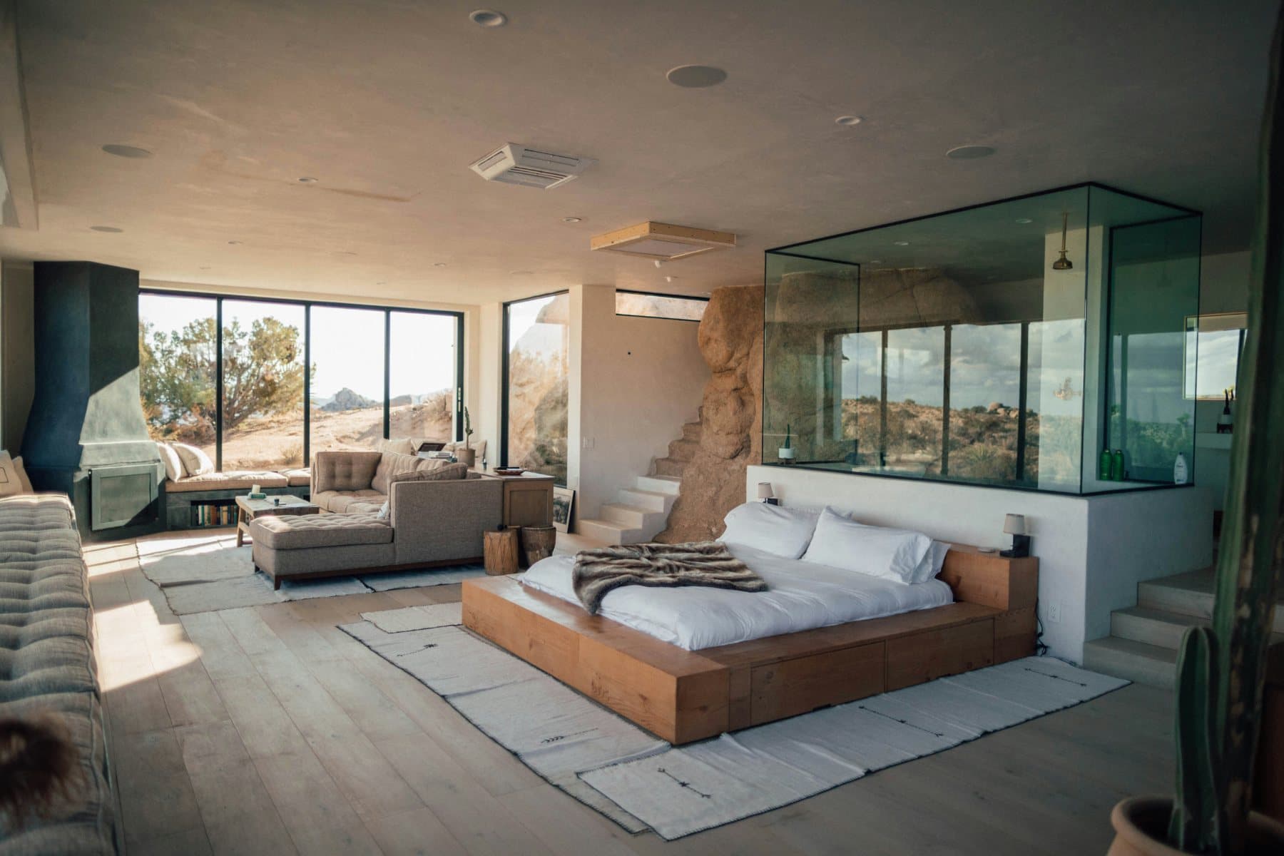 A glass-walled bath and bedroom finished in natural stone